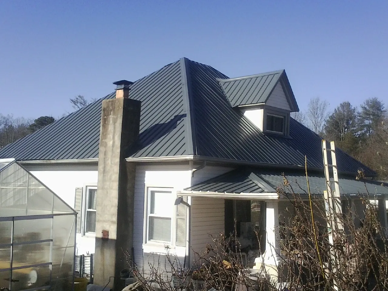 Dark blue standing seam metal roof on a white farmhouse with dormer — Slate & Tile Roof Repair by Roofing Brothers in Fields