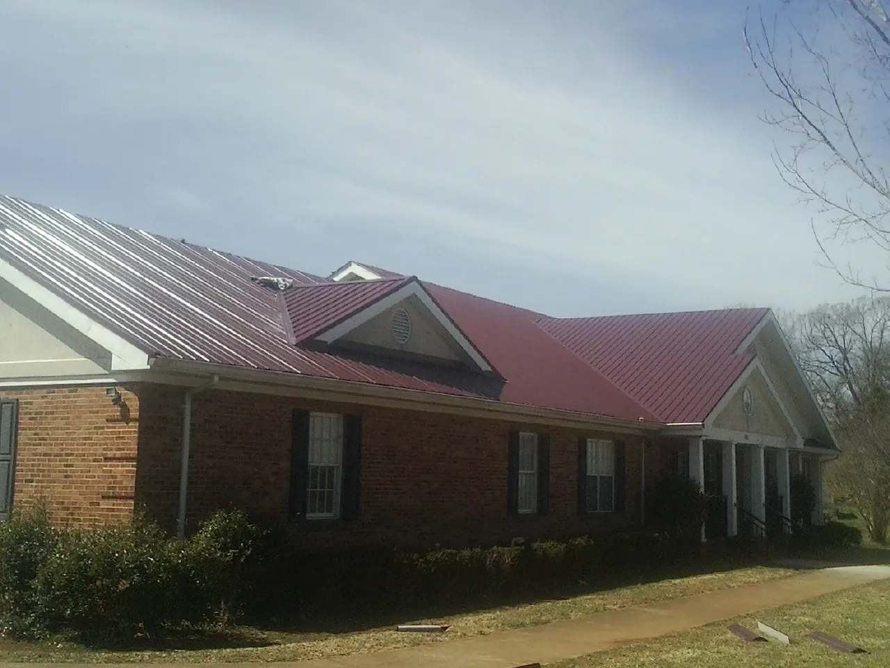 Red metal roof with gabled entries on a long brick building, from a Hail Damage Roof Repair job in Fields